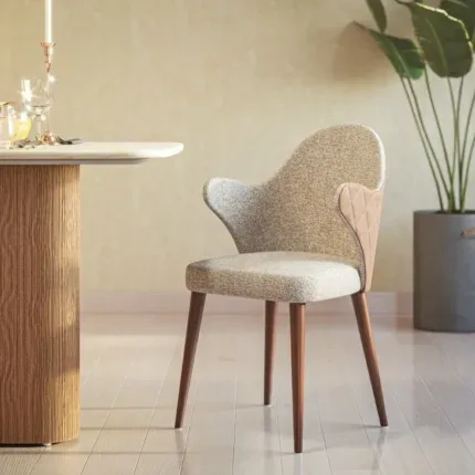 Modern upholstered dining arm chair with curved backrest, mustard fabric, black legs, and gold-tipped feet beside a round dining table.