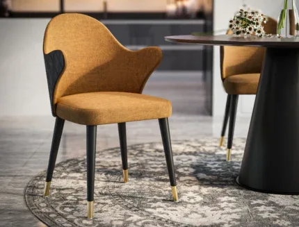Luxury upholstered dining arm chair featuring a wraparound backrest and gold-capped legs in a modern dining room.