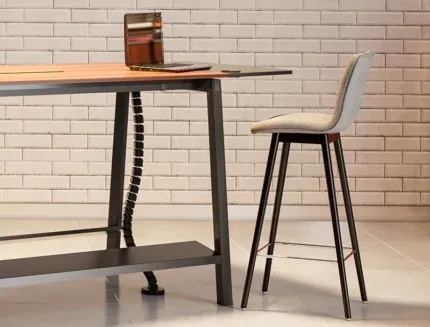 Modern upholstered fabric bar stool with black metal legs beside a contemporary wooden workspace and brick wall background.